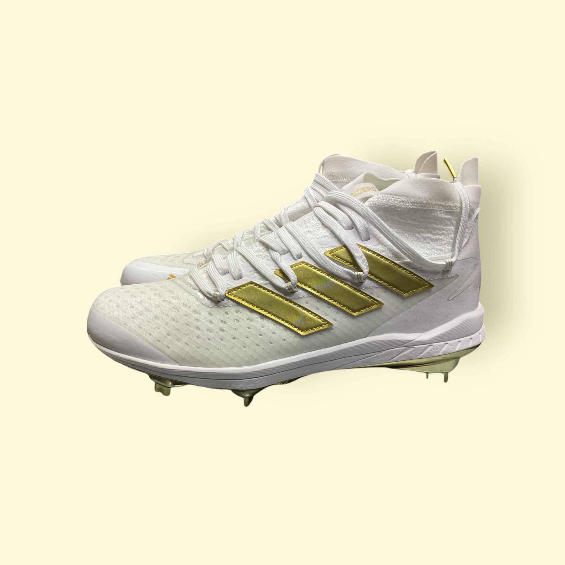Zapatillas de béisbol Adizero Afterburner 8 NWV en blanco y dorado, ligeras y transpirables, diseñadas para velocidad y tracción óptima en el campo
