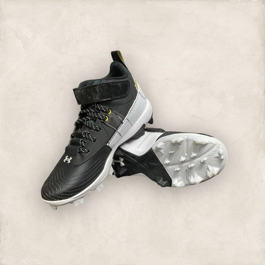 Zapatillas UA Harper 7 Mid RM Jr en negro y dorado, ideales para béisbol, con diseño moderno, parte superior ligera y suela de goma para un agarre superior.