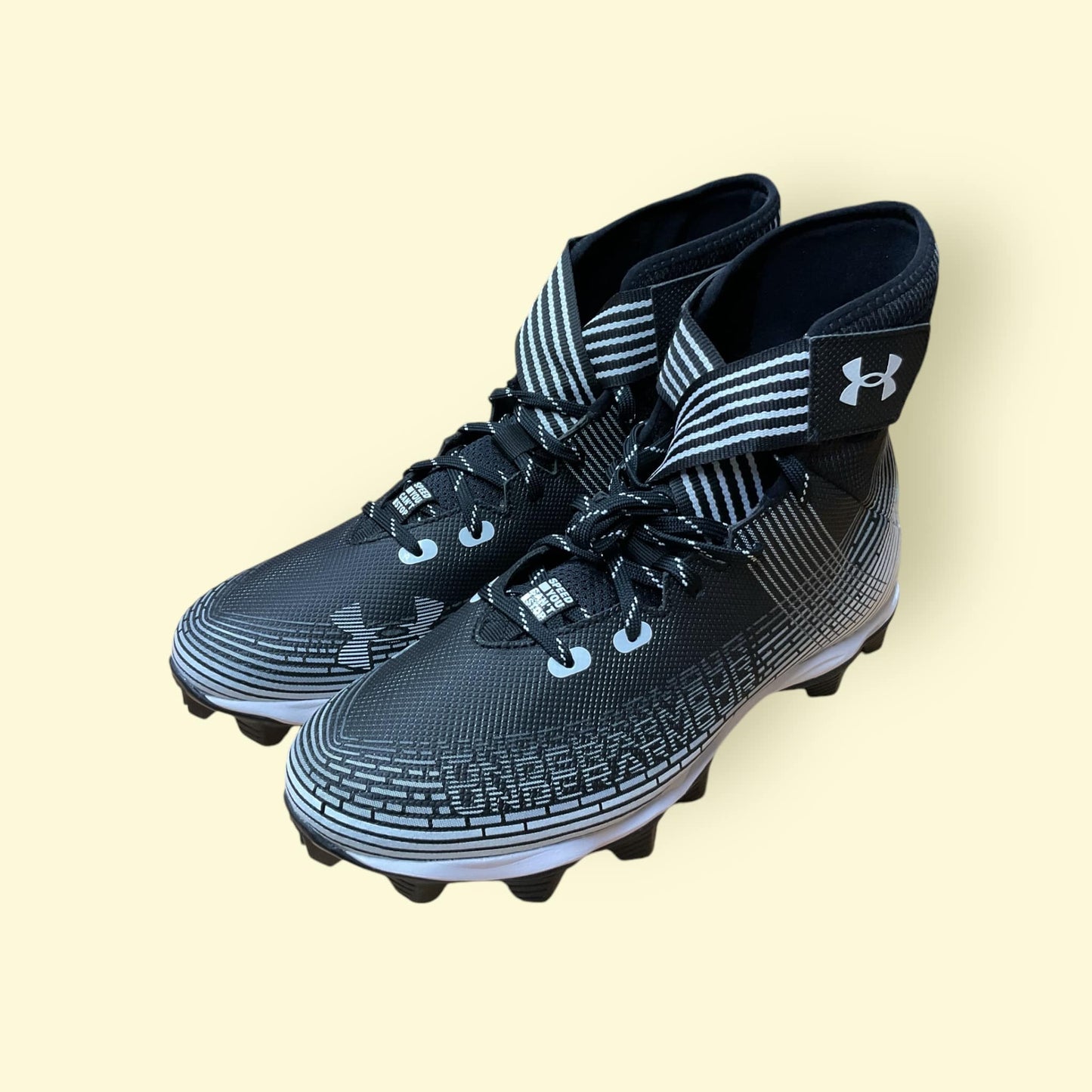 Tacos deportivos UA Highlight Franchise negros para béisbol y fútbol, con soporte en tobillo y suela de tracción.