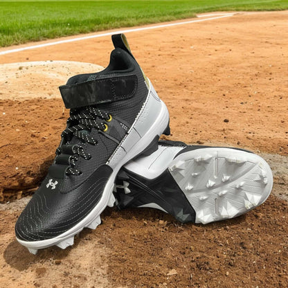 Zapatillas UA Harper 7 Mid RM Jr en negro y dorado, ideales para béisbol, con diseño moderno, parte superior ligera y suela de goma para un agarre superior.